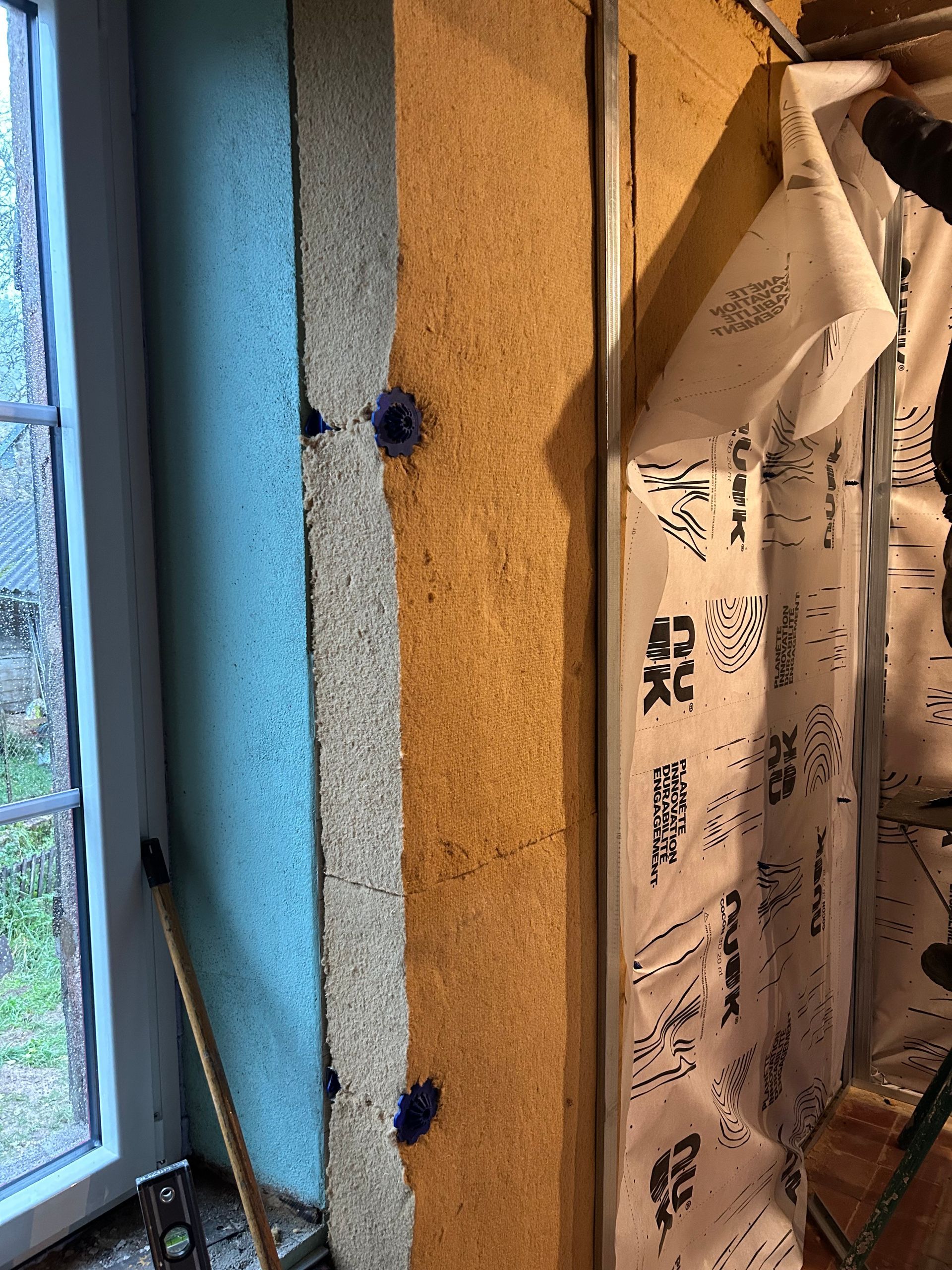 Couches de construction du mur : isolant bleu, panneau de fibres de bois, montants métalliques avec pare-vapeur.
