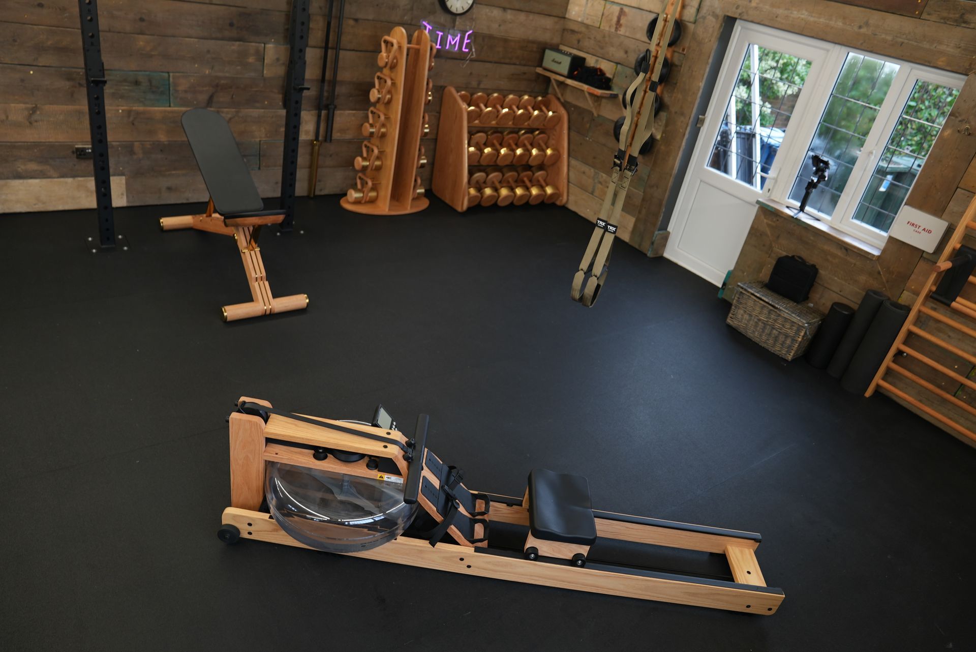 A wooden rowing machine is sitting on a black floor in a gym.