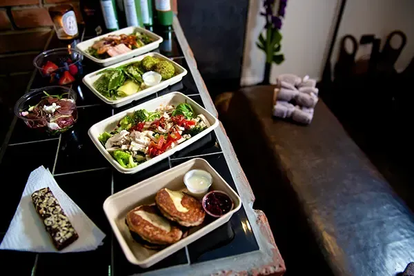 A table topped with trays of food including salads and sandwiches.