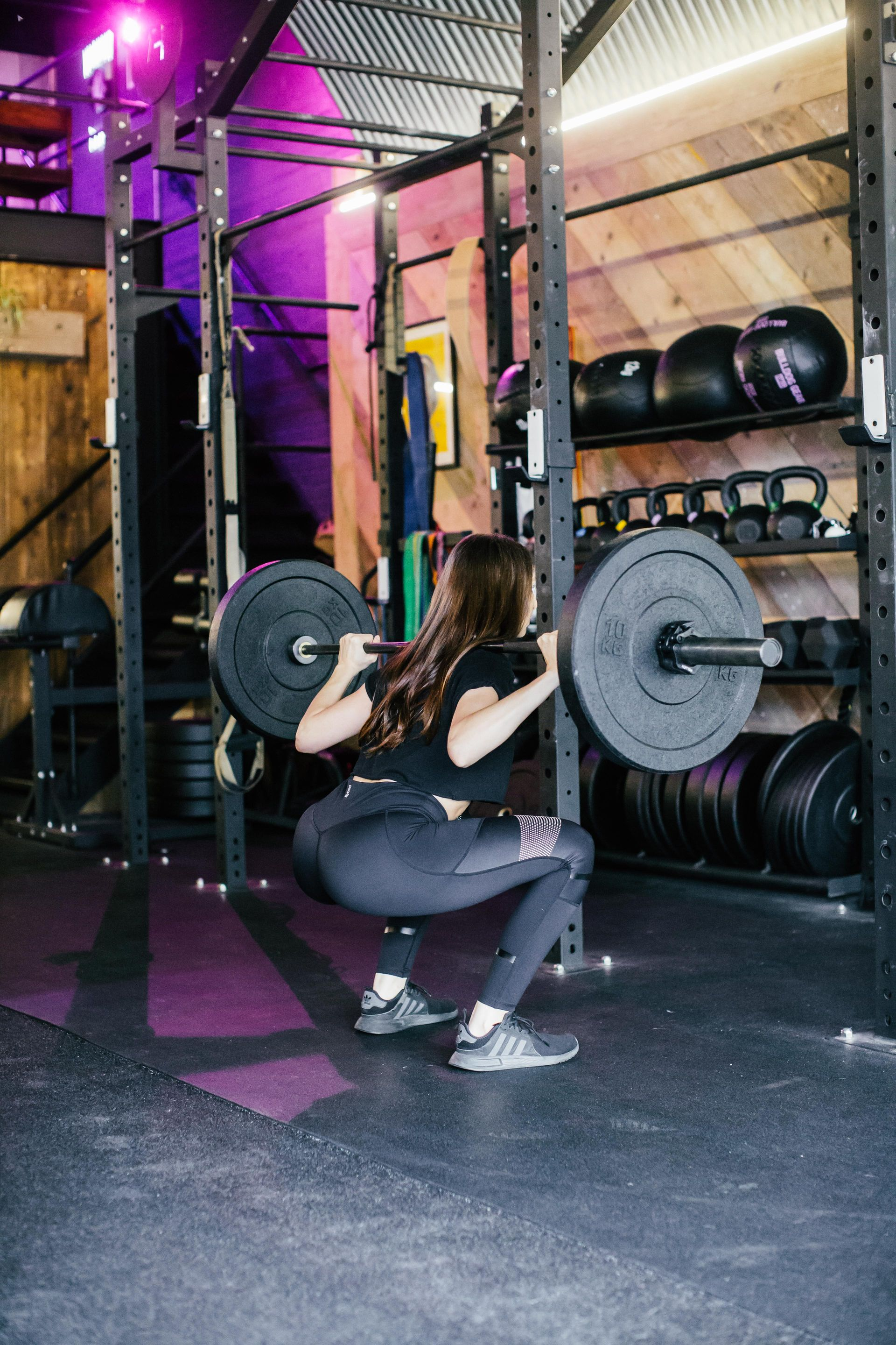 Woman doing a barbell squat in a gym, wearing black activewear.
