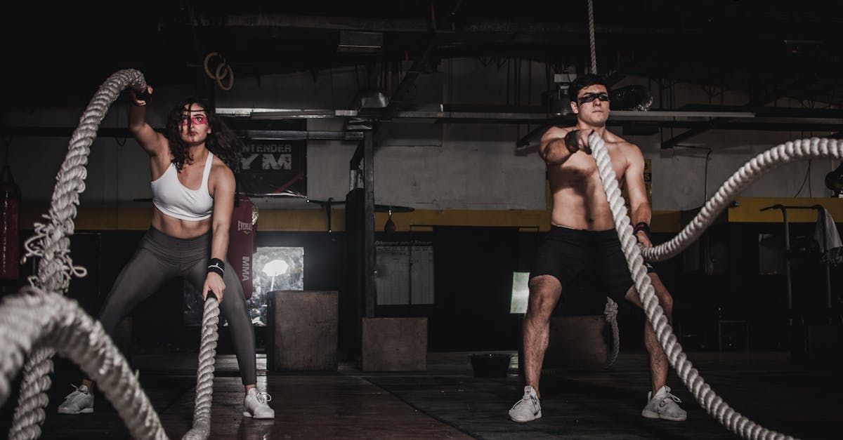 A man and a woman are holding ropes in a gym.