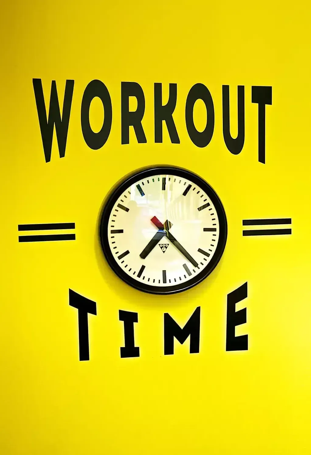A clock on a yellow wall that says workout time