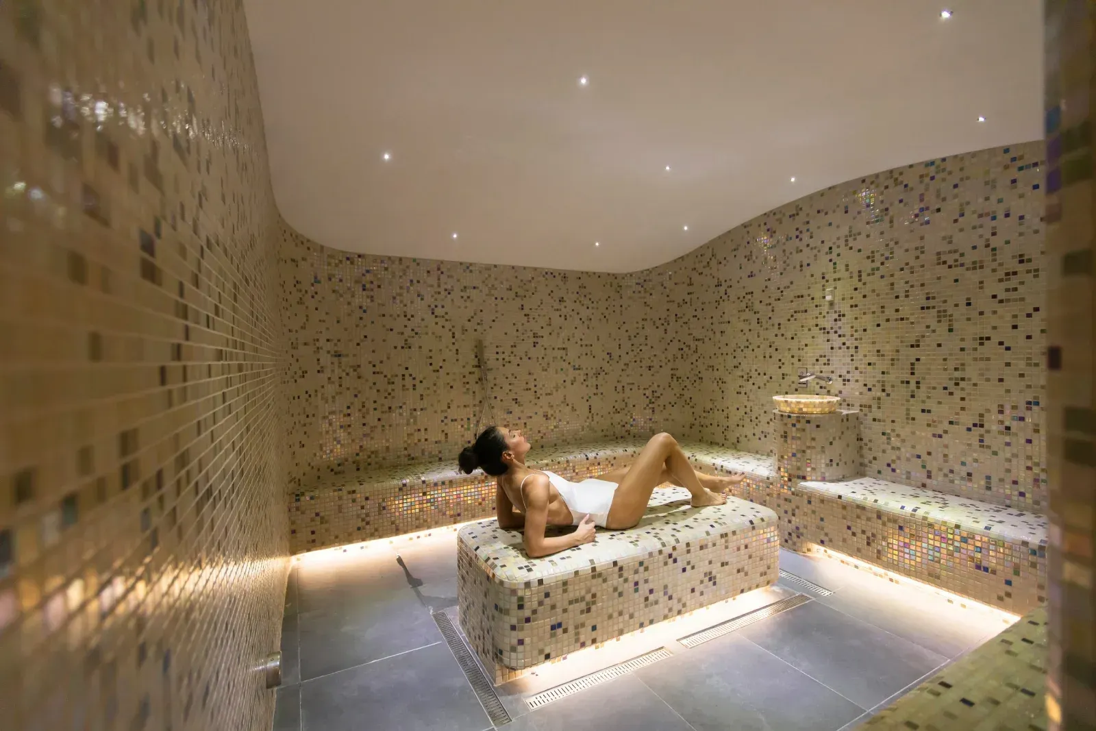 Mujer relajándose en un baño de vapor con mosaicos, reclinada en un banco, 