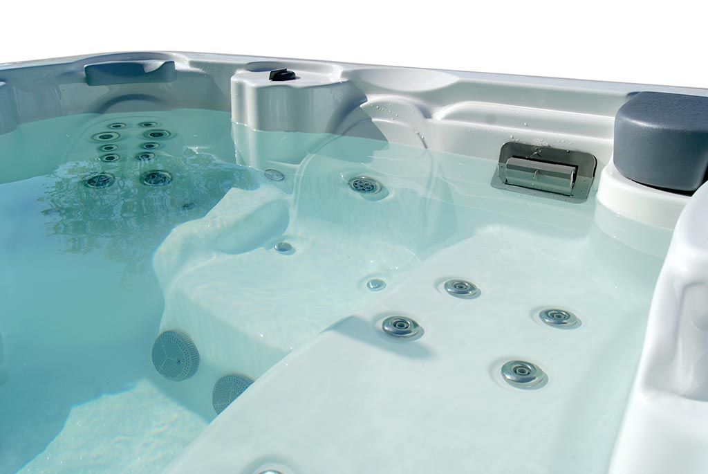 Bañera de hidromasaje blanca llena de agua clara, chorros visibles, agua fluyendo, luz solar.