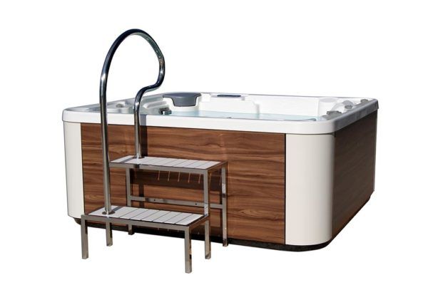 Bañera de hidromasaje con escalones incorporados y pasamanos, rodeada de paneles de madera, lista para su uso.