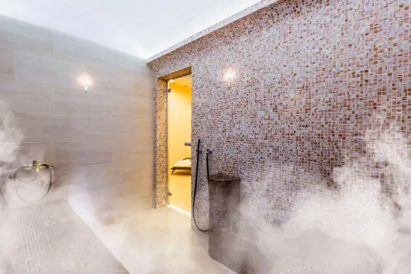 Baño lleno de vapor con paredes de azulejos y puerta abierta que conduce a una zona de ducha.