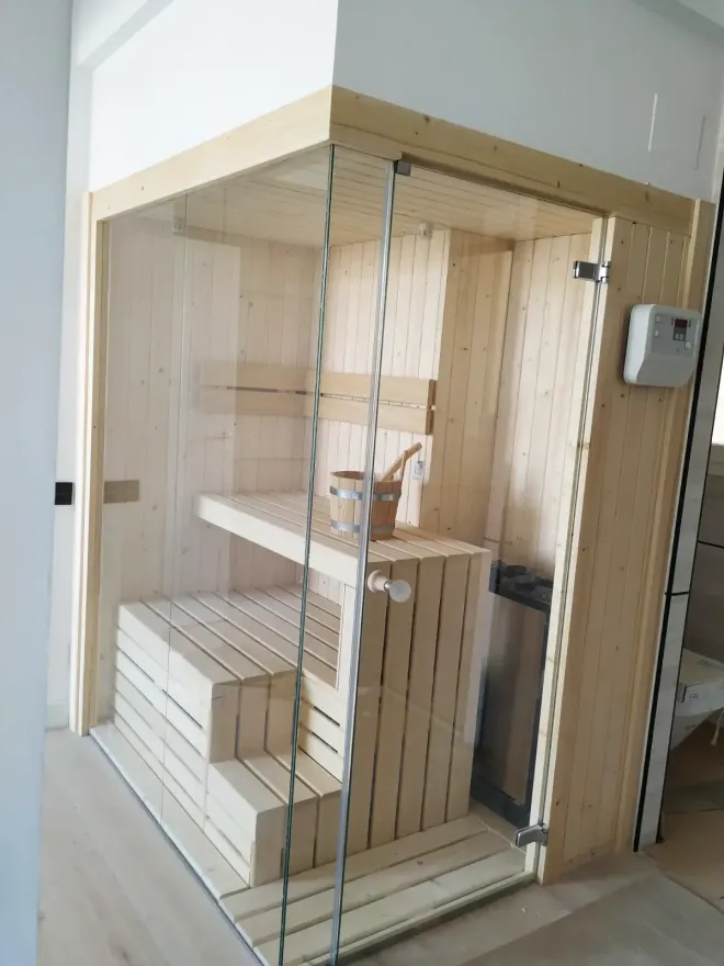 Sauna de madera con puerta de cristal, bancos y cubo.