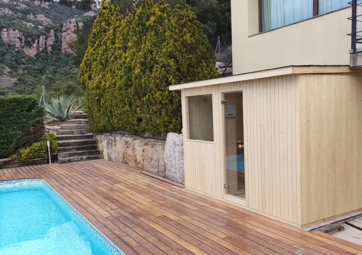 Sauna de madera junto a una piscina en una terraza de madera. 