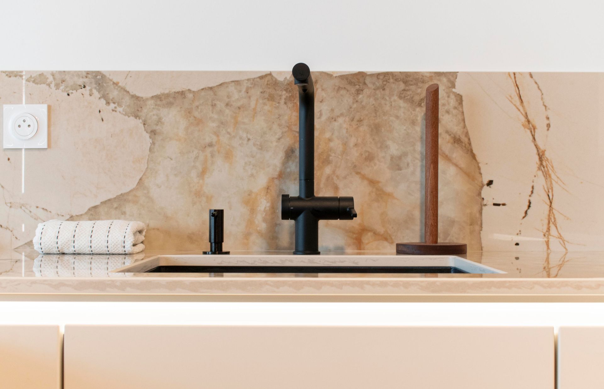 Évier de cuisine moderne avec robinet noir, distributeur de savon, porte-serviettes en papier et dosseret en marbre.