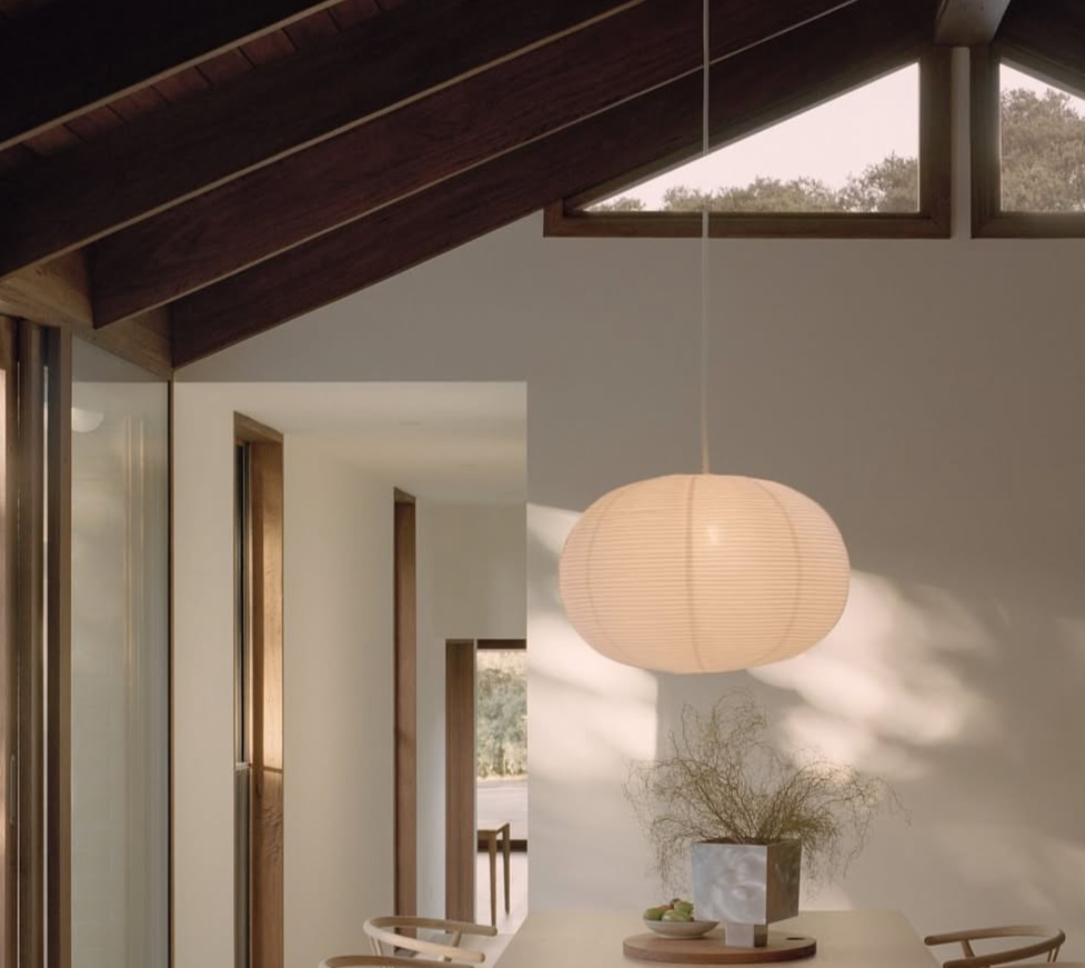 Bureau à domicile aux tons neutres avec un bureau en bois, une chaise blanche, des lampes suspendues et des rideaux beiges.
