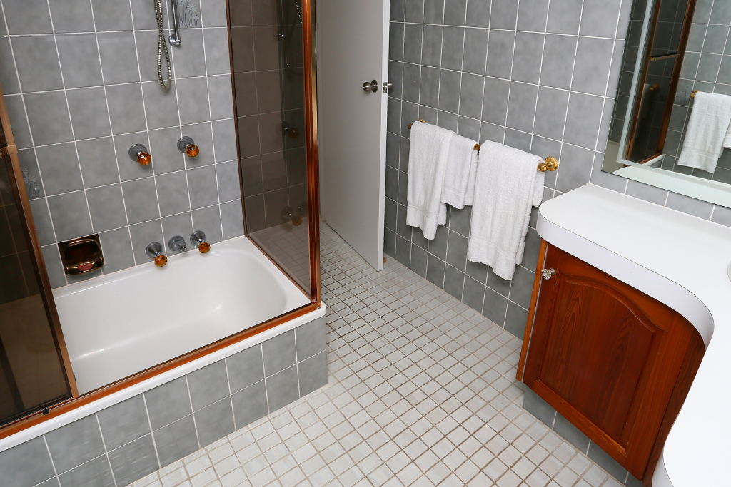 Salle de bain avec baignoire blanche, murs carrelés gris et vanité en bois.