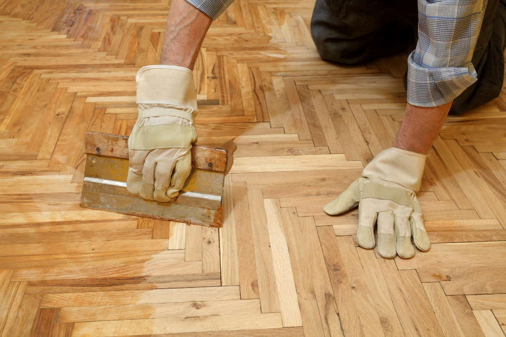 Personne appliquant la finition sur un parquet à l'aide d'une brosse et portant des gants.