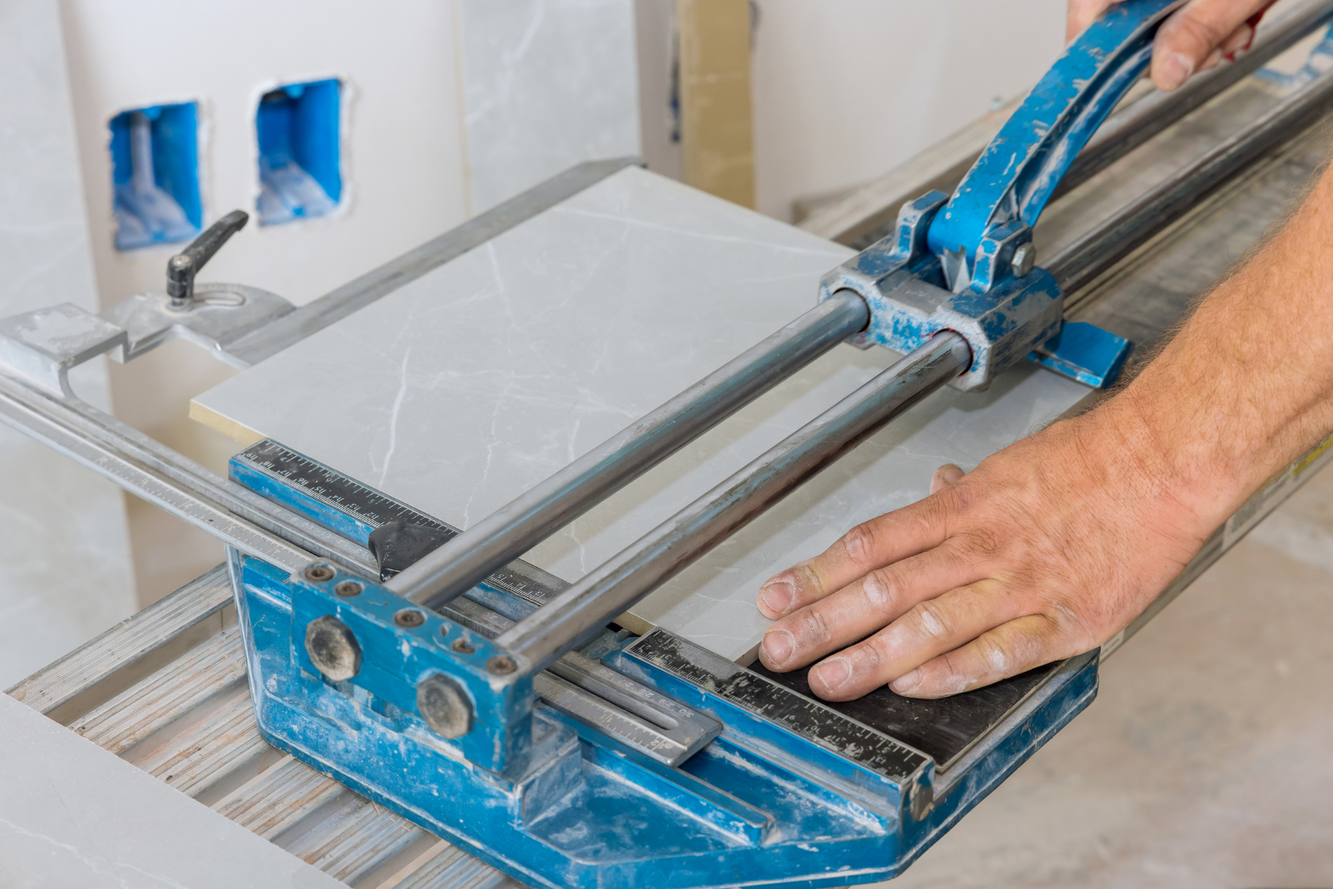 Homme coupant une tuile avec un coupe-carreaux bleu ; tuile blanche, cadre intérieur.