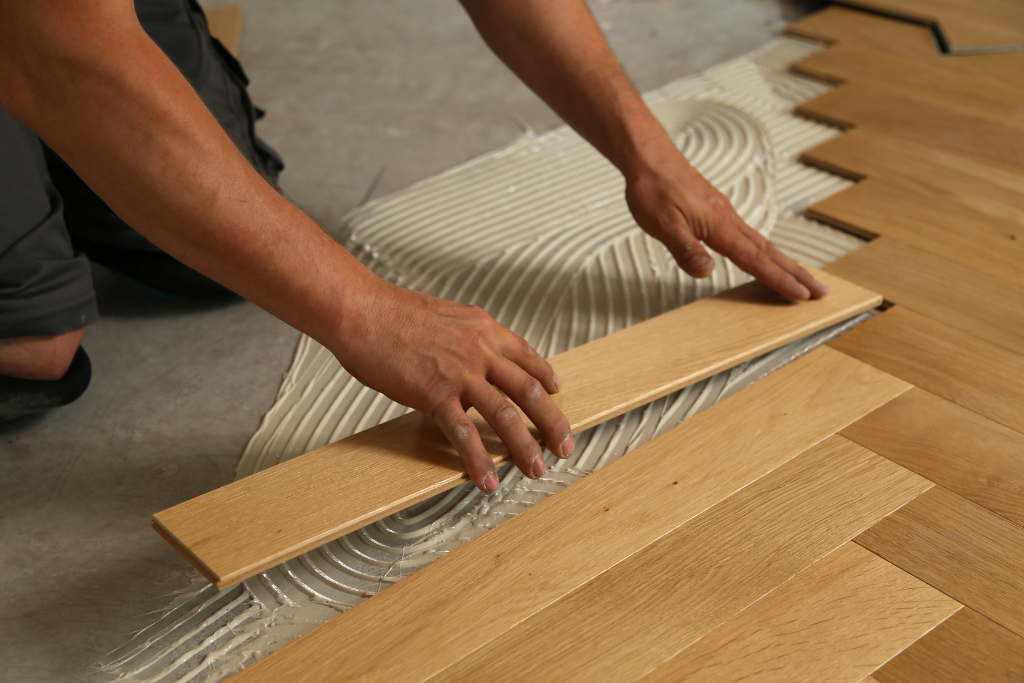 Personne installant du parquet, appliquant de la colle sur le sous-plancher, posant des planches de bois.