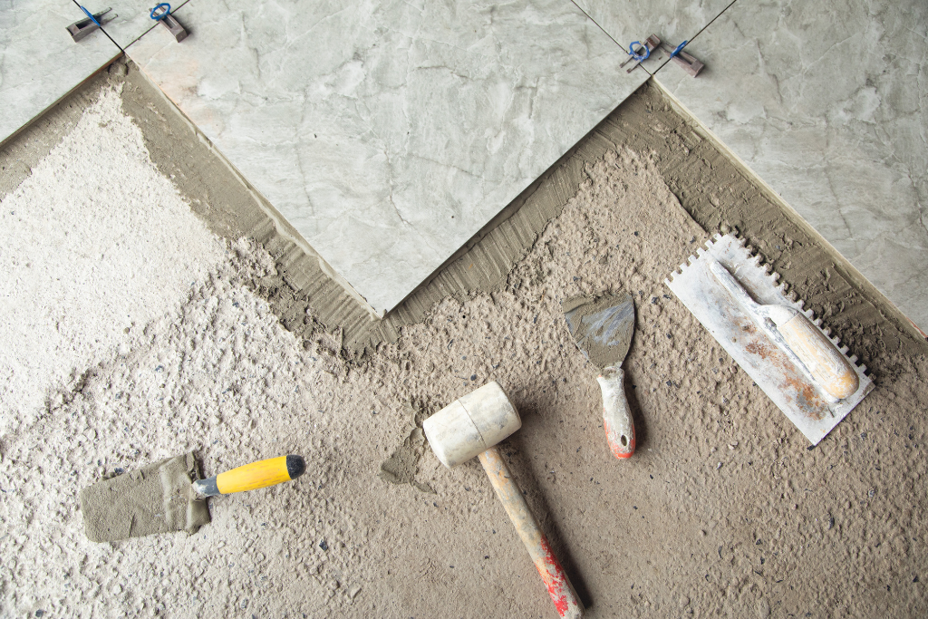 Carrelage en cours : les carreaux sont posés avec du mortier, des outils comme des truelles et un maillet sont visibles.