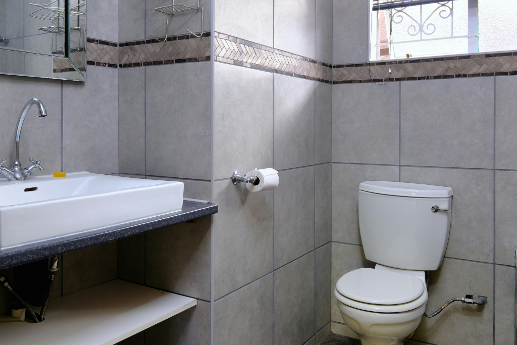 Salle de bain avec lavabo blanc, toilettes et murs carrelés.