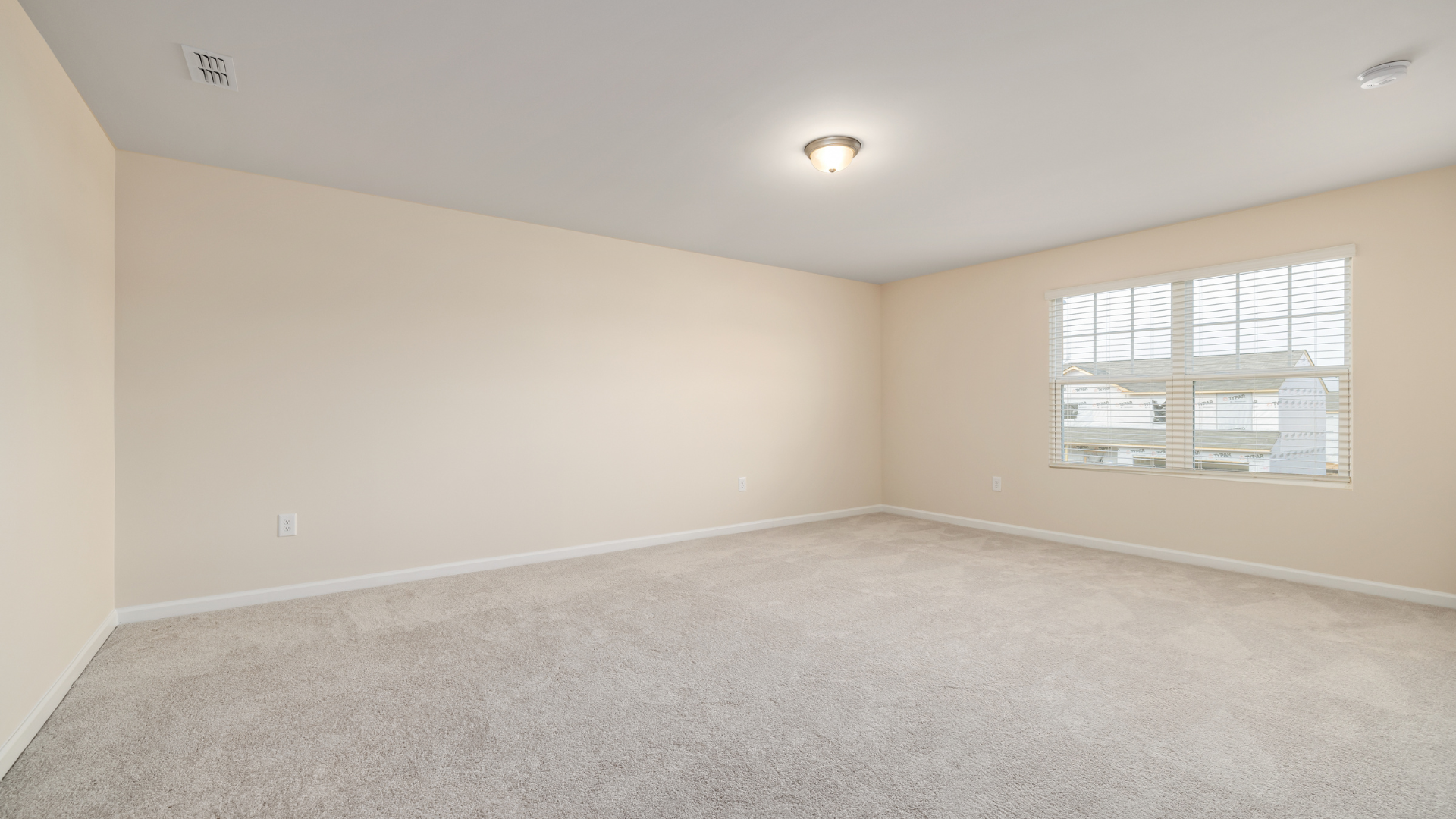 Chambre vide avec murs beiges, tapis clair et fenêtre.