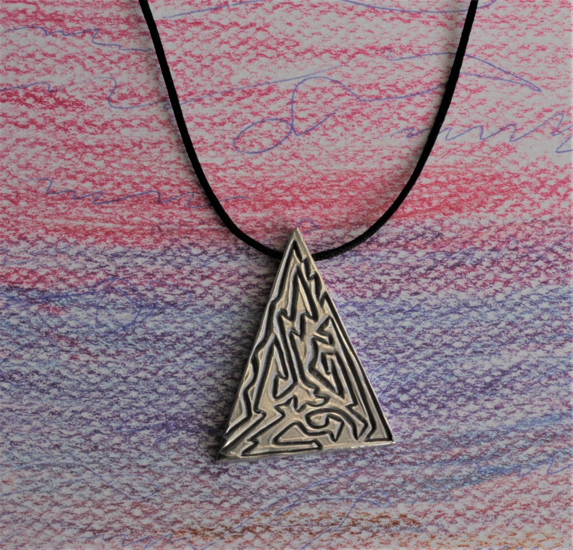 Un collar con un colgante en forma de triángulo en un cordón negro.