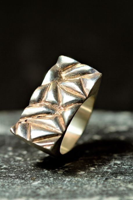 Un anillo de plata y oro reposa sobre una superficie negra.