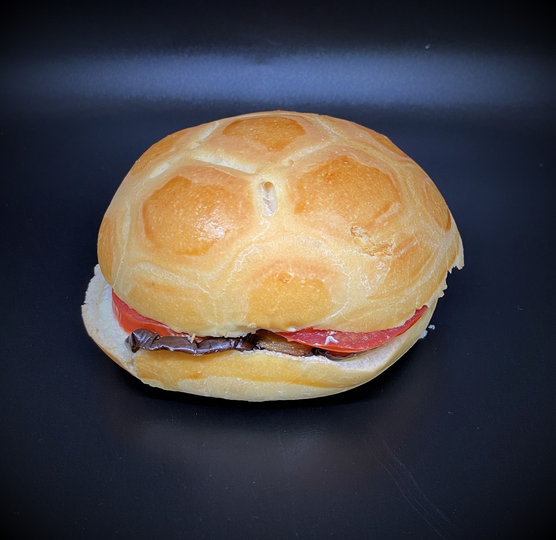 Sandwich à la tomate et à la garniture, sur un pain rond. Fond sombre.