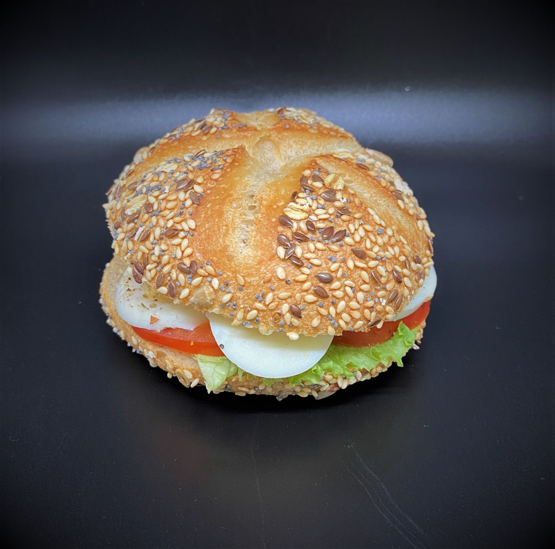 Sandwich sur pain aux graines, avec laitue, tomate et œuf. Fond noir.