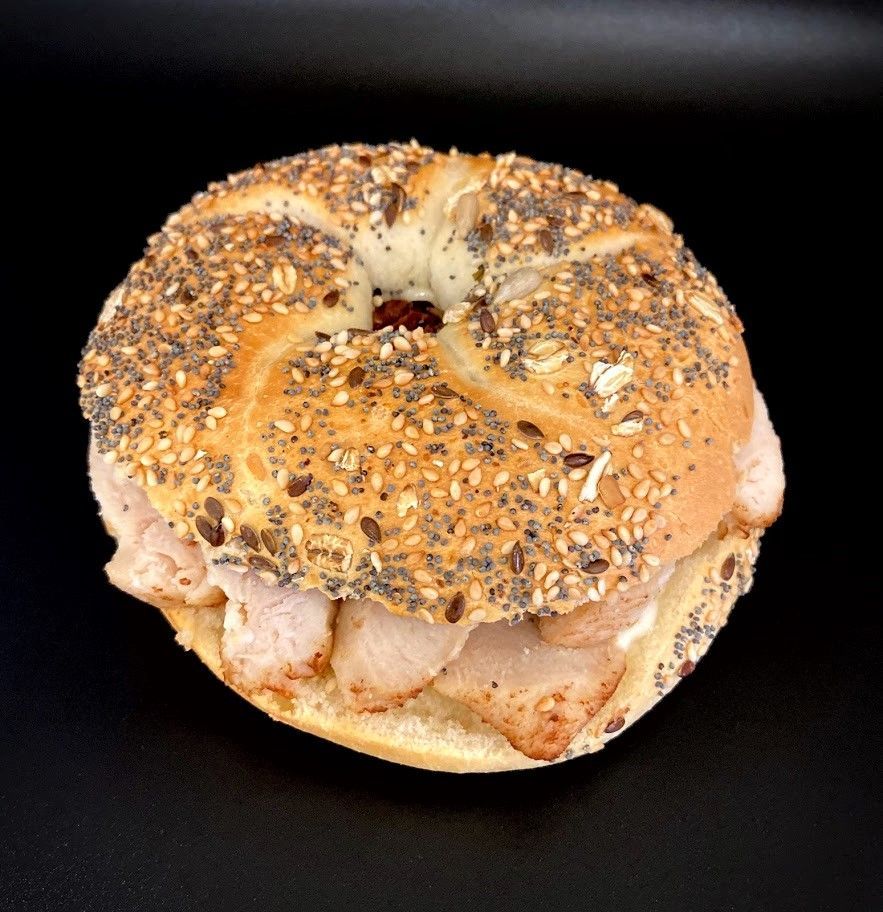 Sandwich bagel tout garni de viande tranchée, sur fond noir.