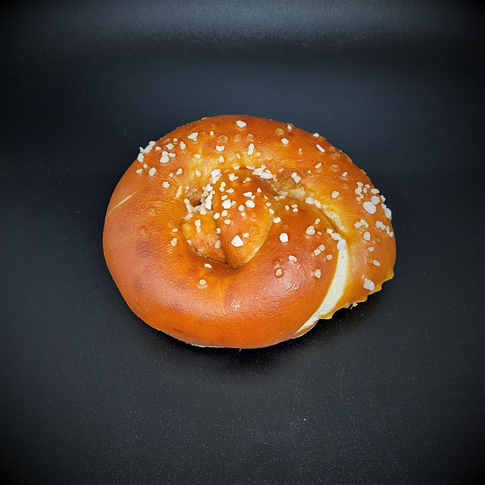 Bretzel moelleux, salé, sur fond noir.