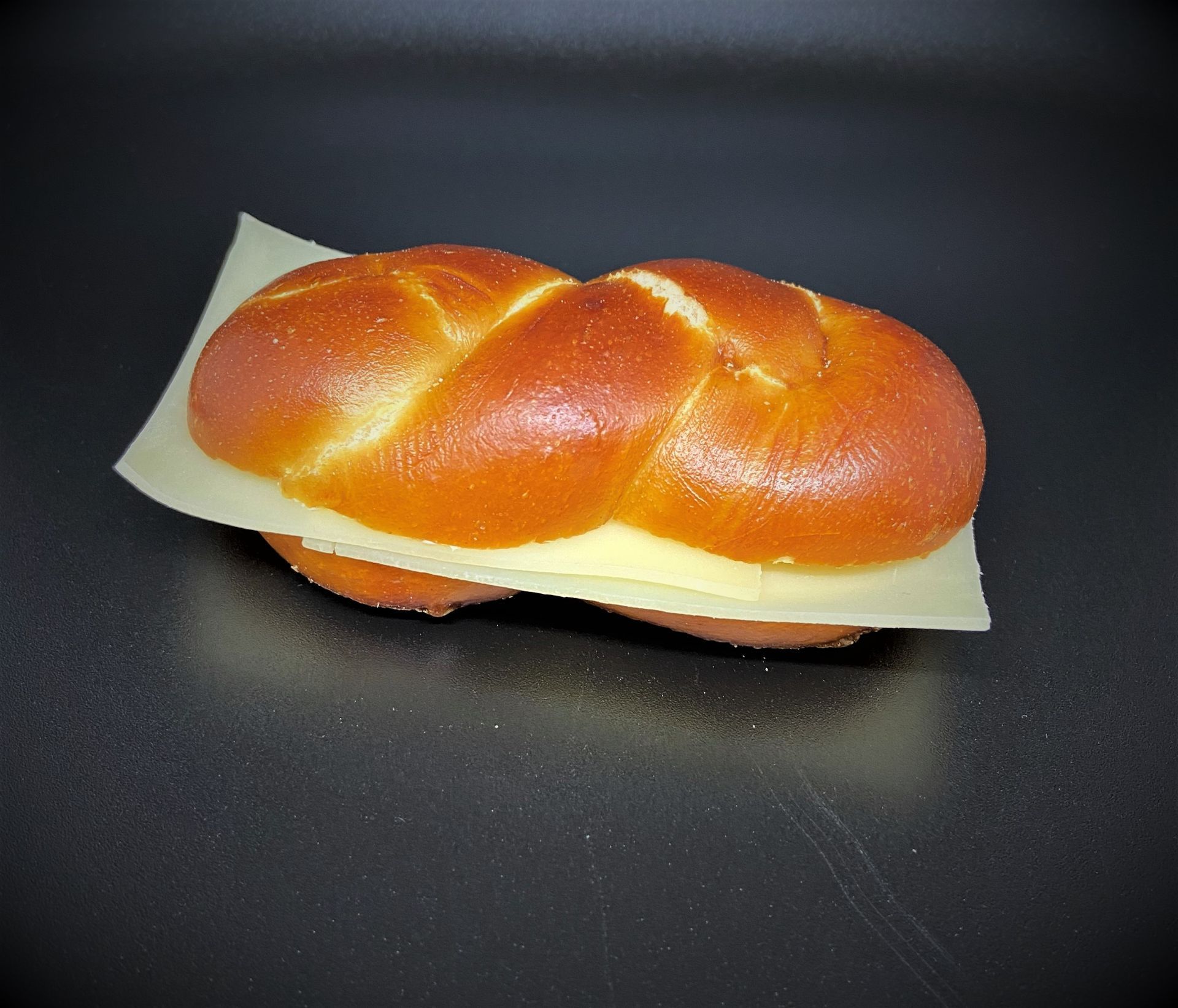 Rouleau tressé avec une tranche de fromage sur une surface noire.