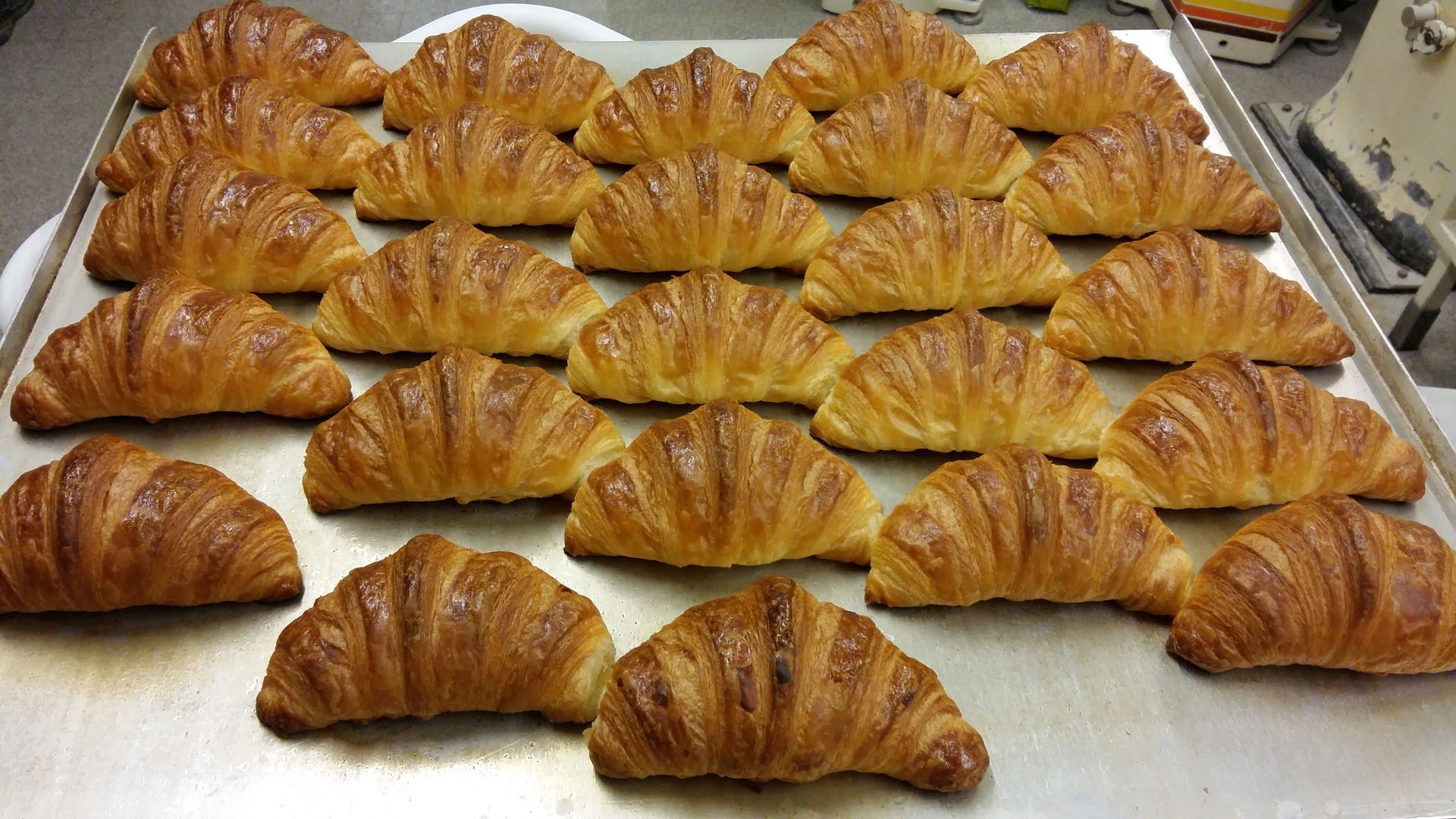 Des rangées de croissants dorés sur une plaque à pâtisserie, prêts à être exposés ou vendus.
