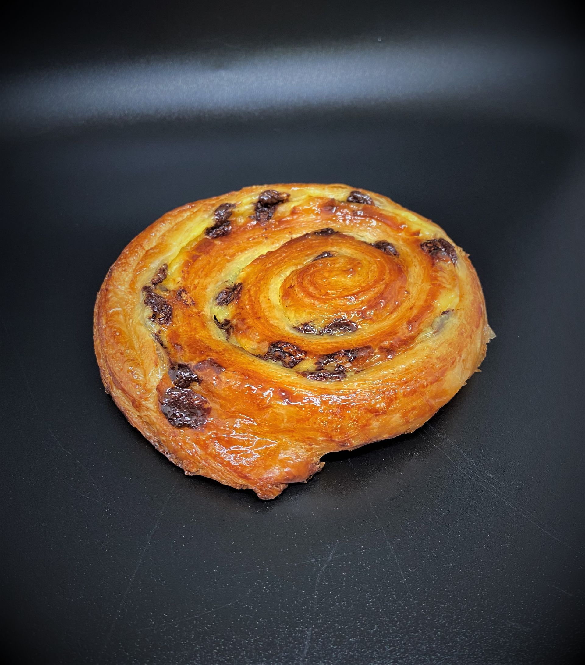 Pâte tourbillonnante aux pépites de chocolat sur une surface foncée, dorée et glacée.