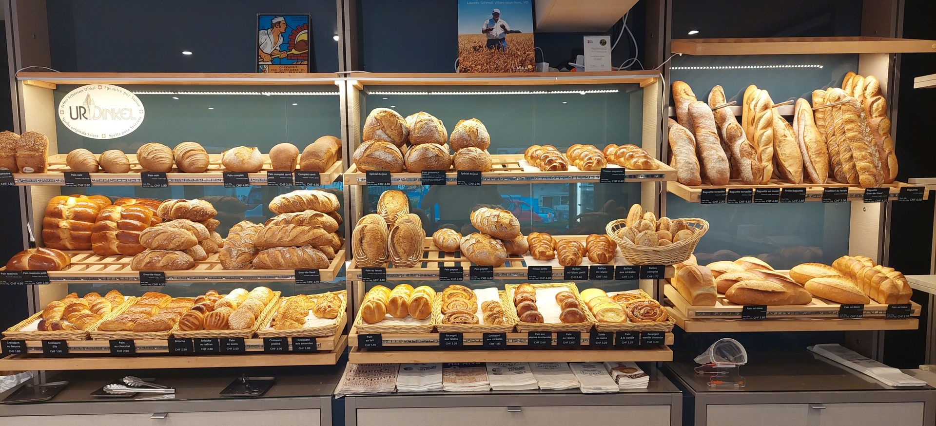 Vitrine de boulangerie : étagères de pains, viennoiseries et pains variés ; éclairage chaleureux, présentoirs en bois.