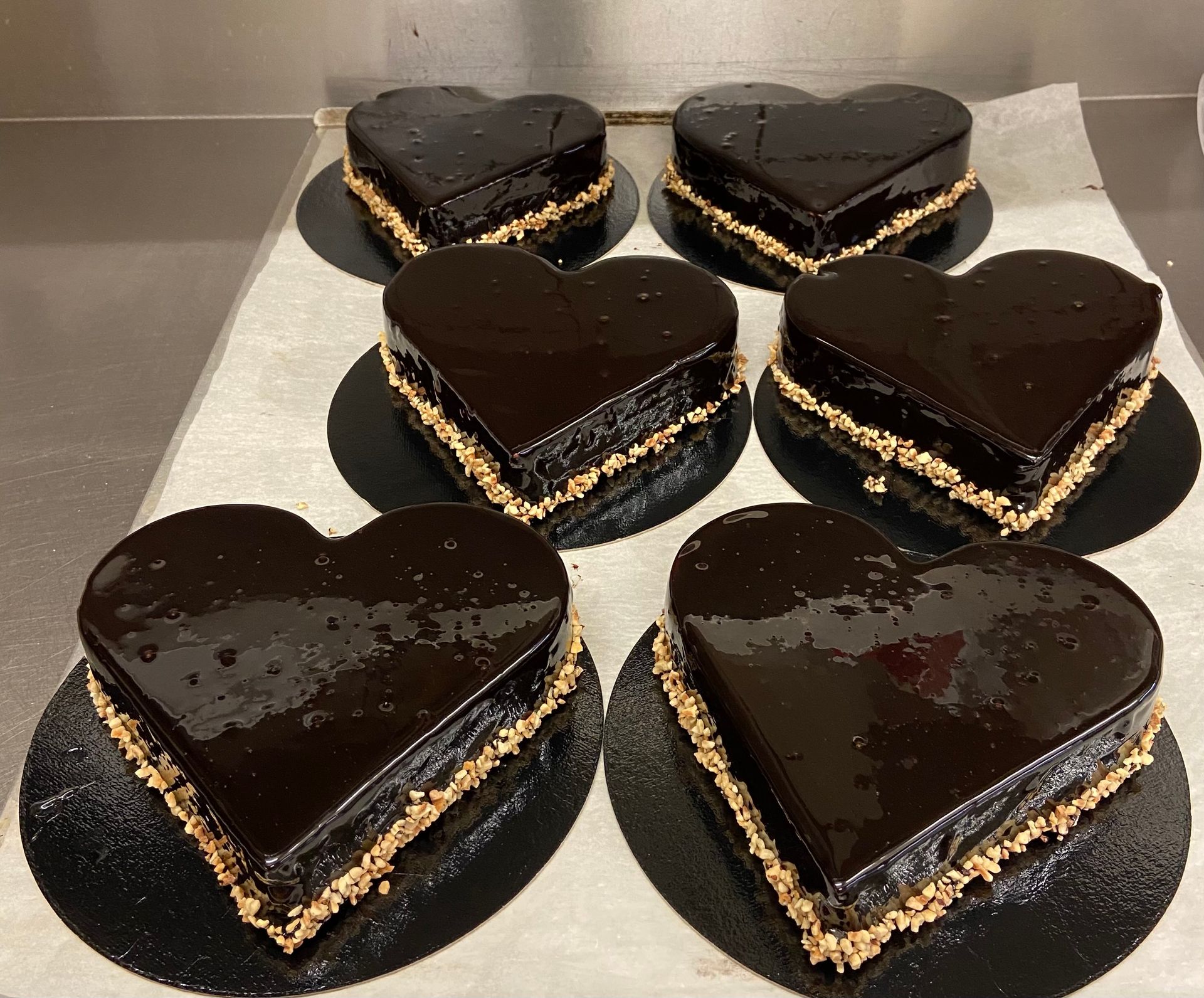 Gâteaux au chocolat en forme de cœur avec un glaçage brillant, garnis de noix, présentés sur des planches circulaires noires.
