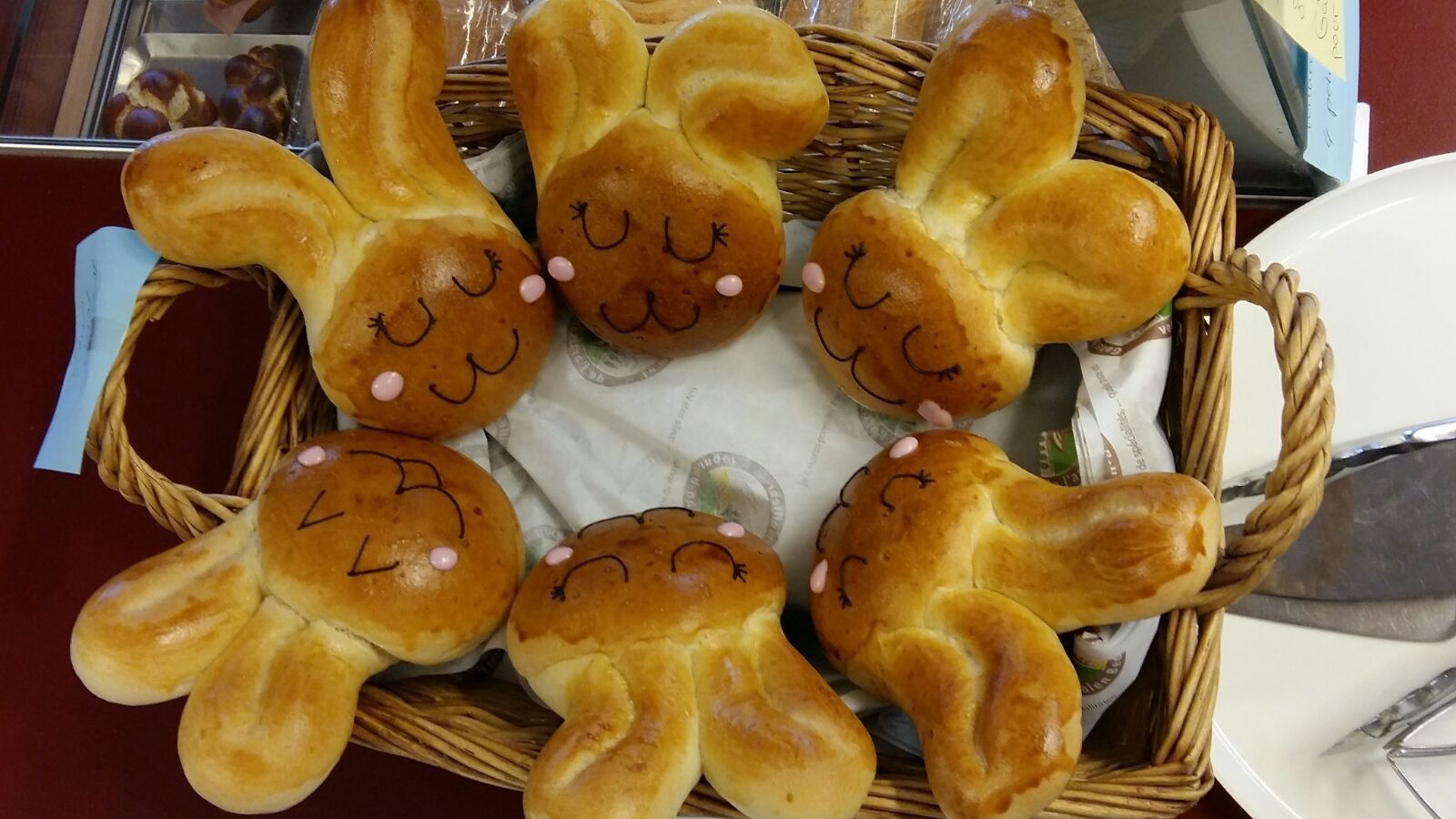 Petits pains en forme de lapin de Pâques dans un panier en osier, avec des visages peints et des nez roses.