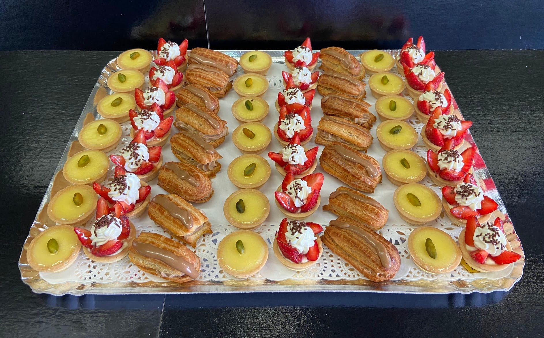 Plateau de pâtisseries assorties : tartes, éclairs et desserts aux fraises, sur un napperon en dentelle.