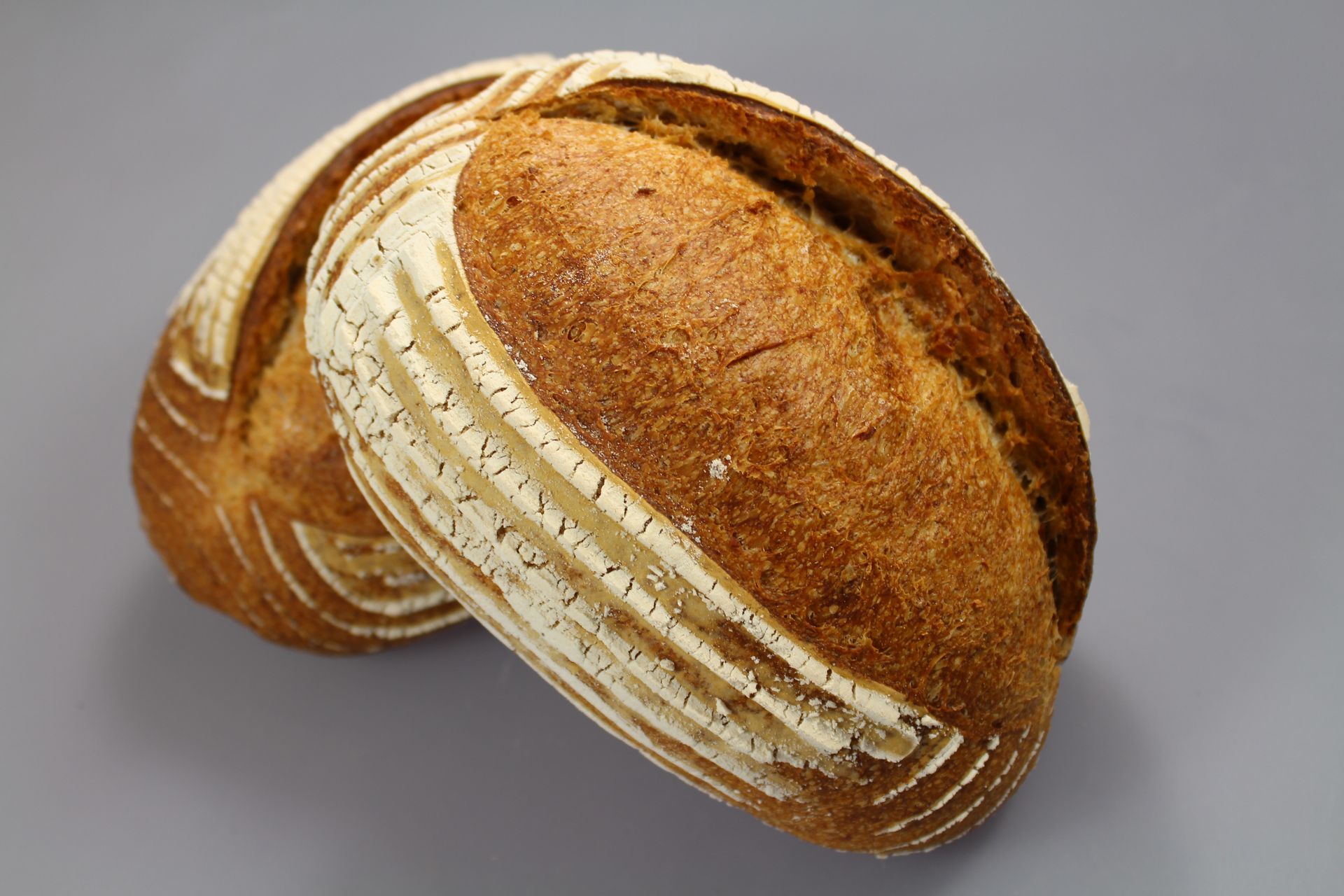 Deux pains rustiques sur une surface grise, avec des dessus rayés et des croûtes brunes.