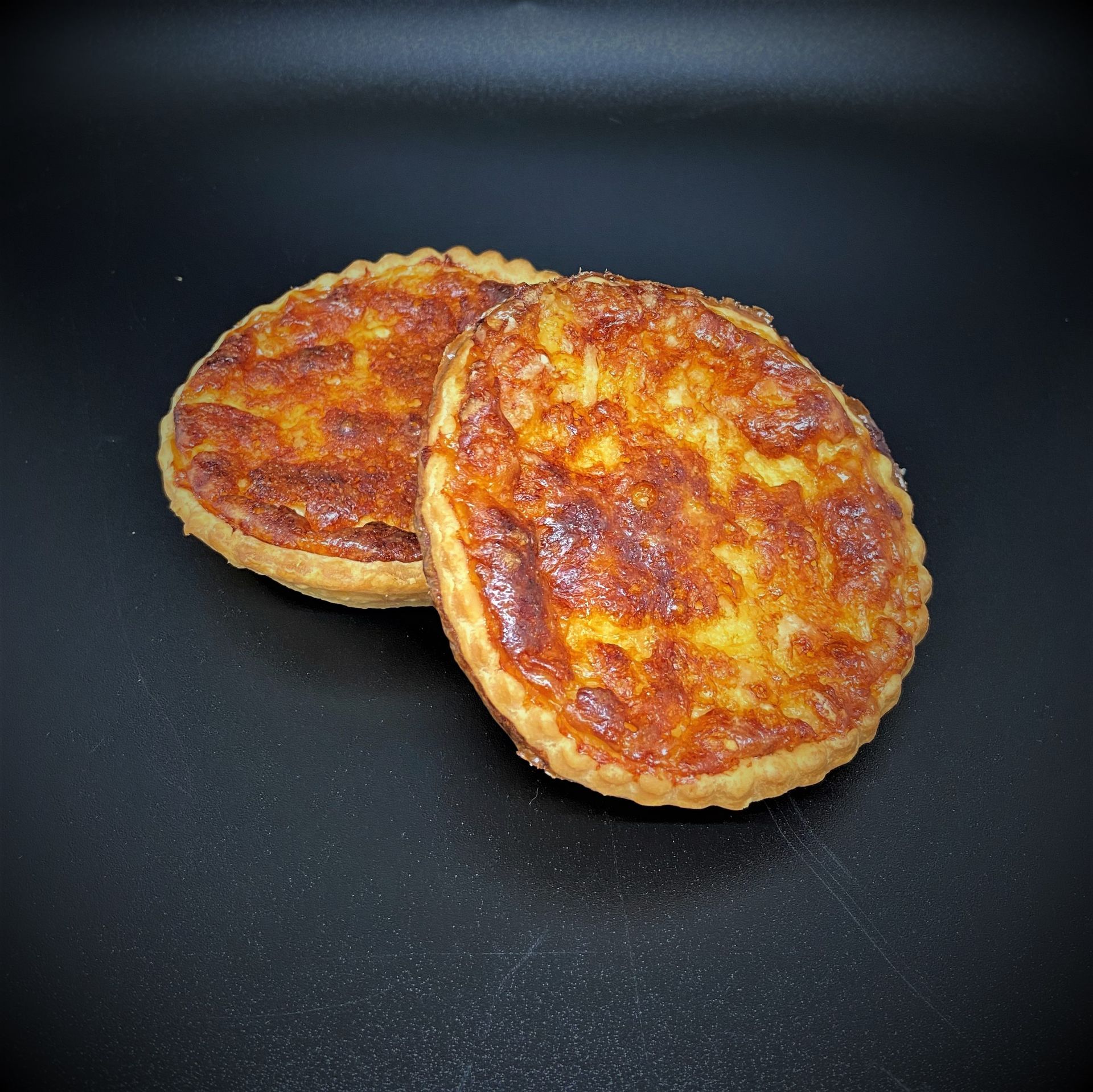 Deux petites quiches dorées sur une surface noire.