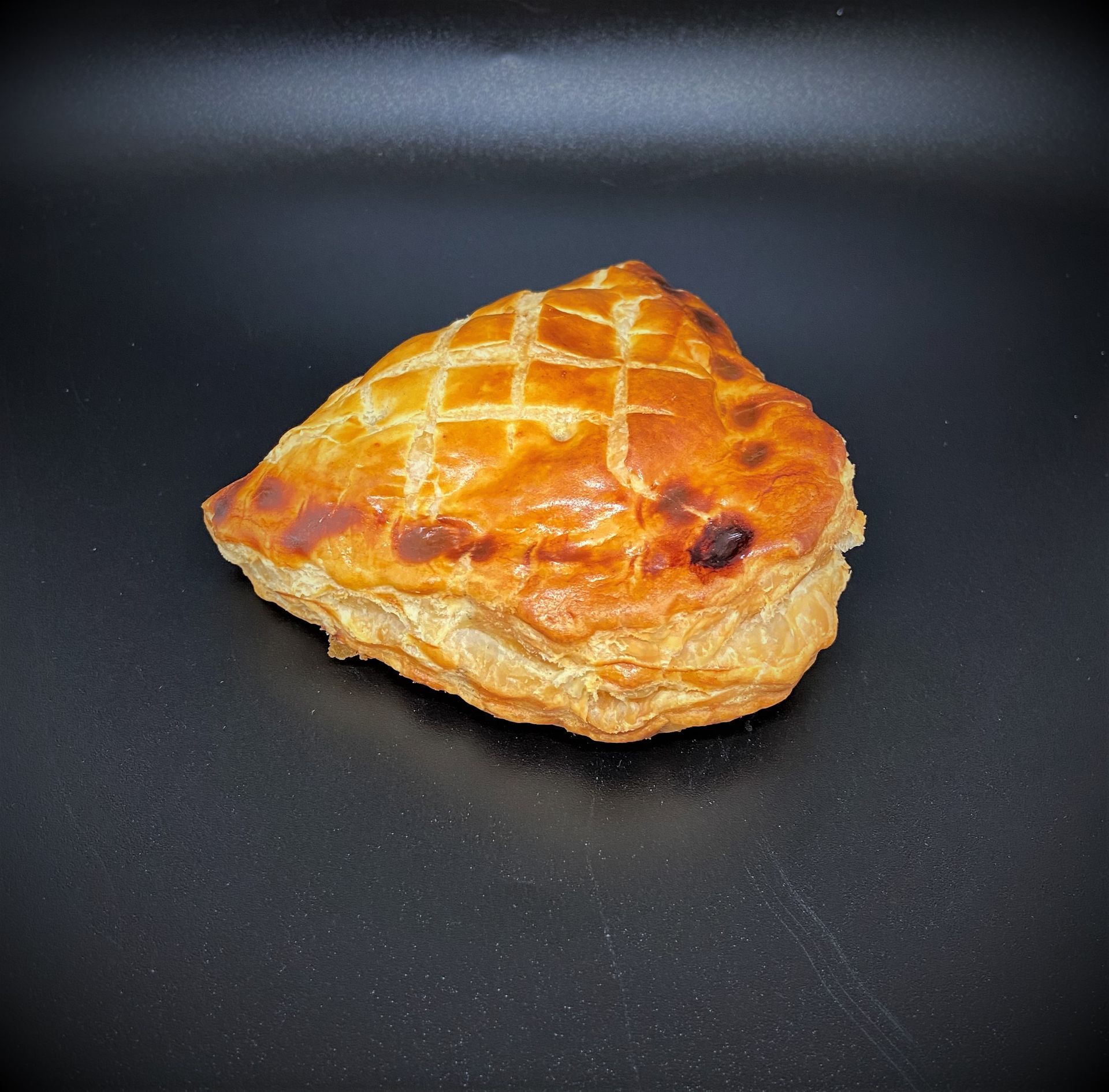 Pâtisserie dorée et cuite au four avec un motif entrecroisé sur le dessus, sur un fond sombre.