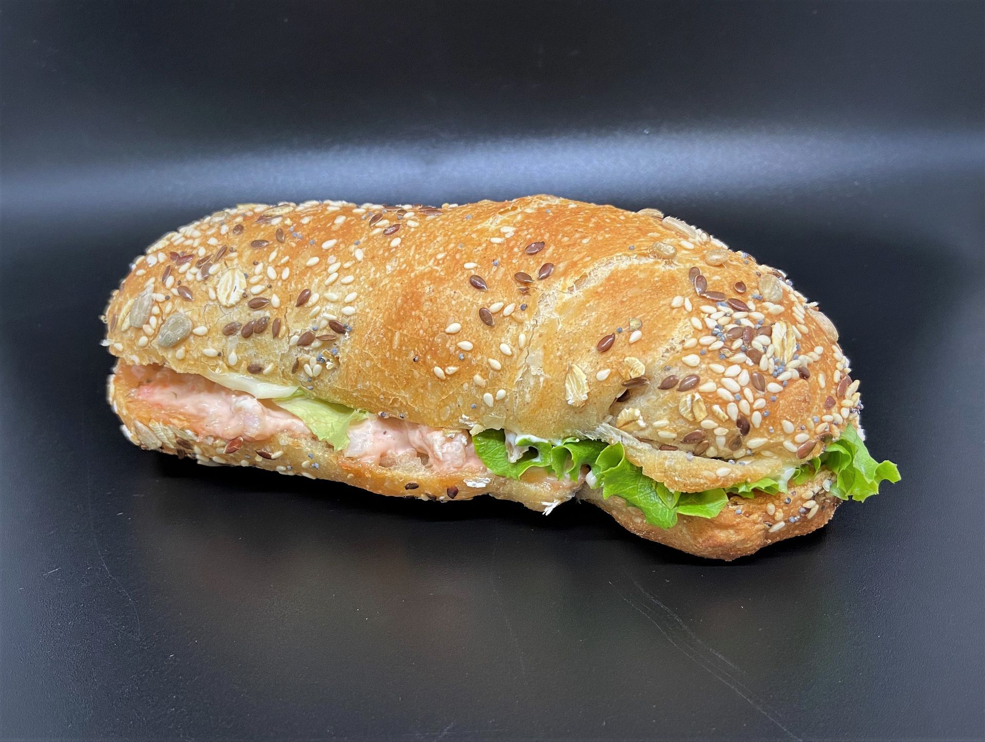 Sandwich au saumon sur un petit pain aux graines avec de la laitue, sur fond noir.