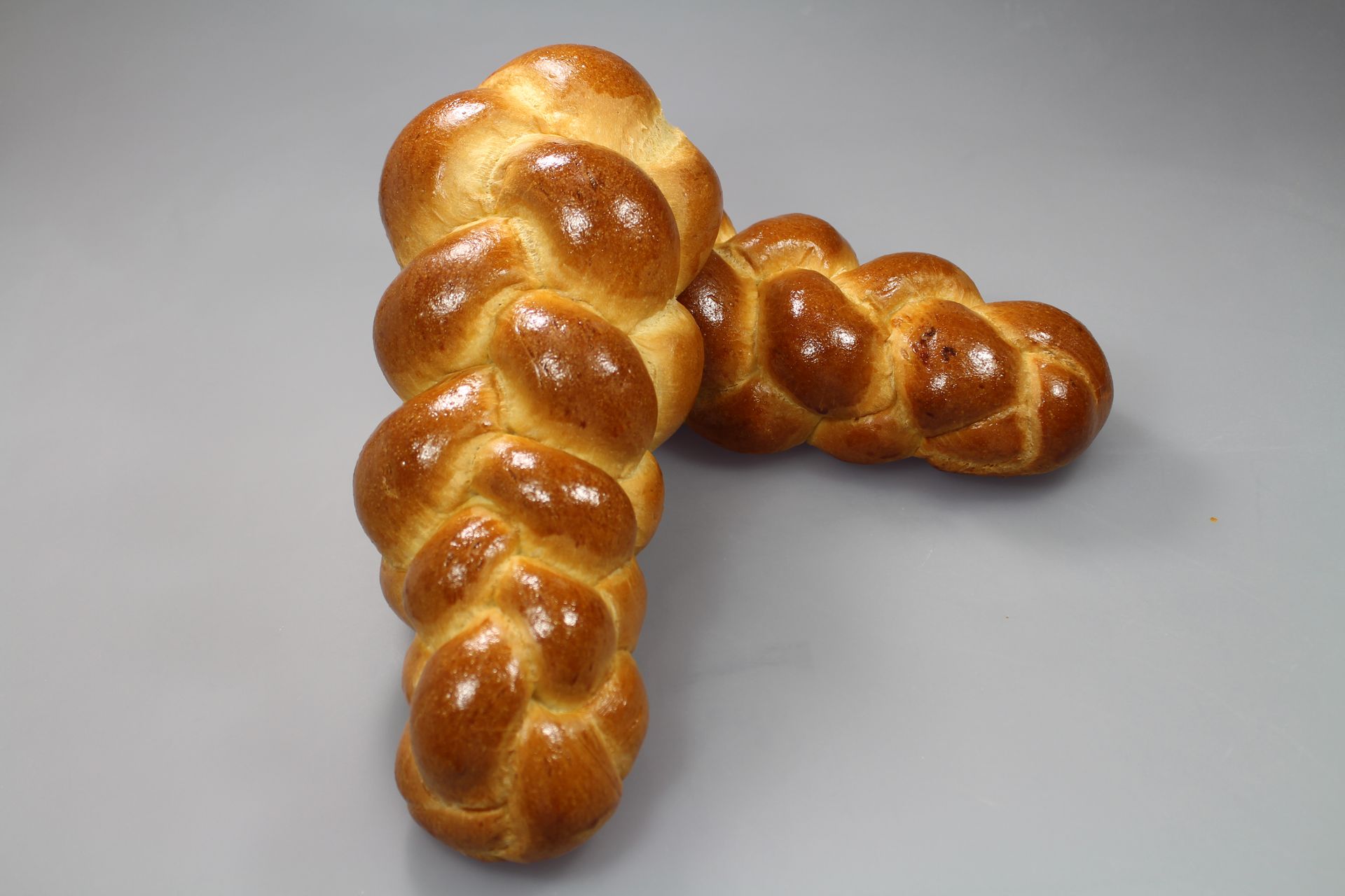 Deux pains challah tressés dorés sur une surface grise.