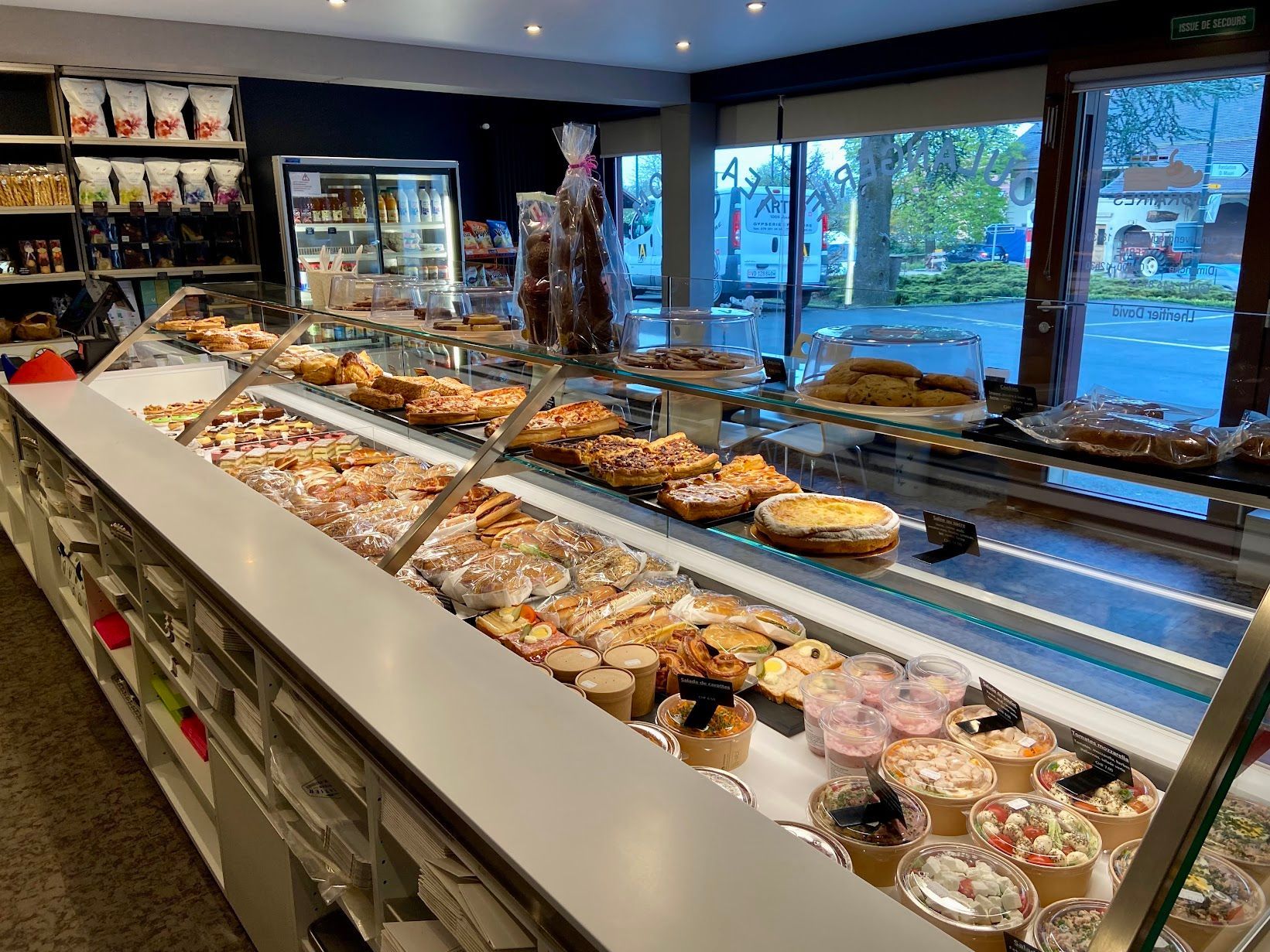 Vitrine de boulangerie remplie de pâtisseries, de gâteaux et de friandises ; les clients ne sont pas visibles.