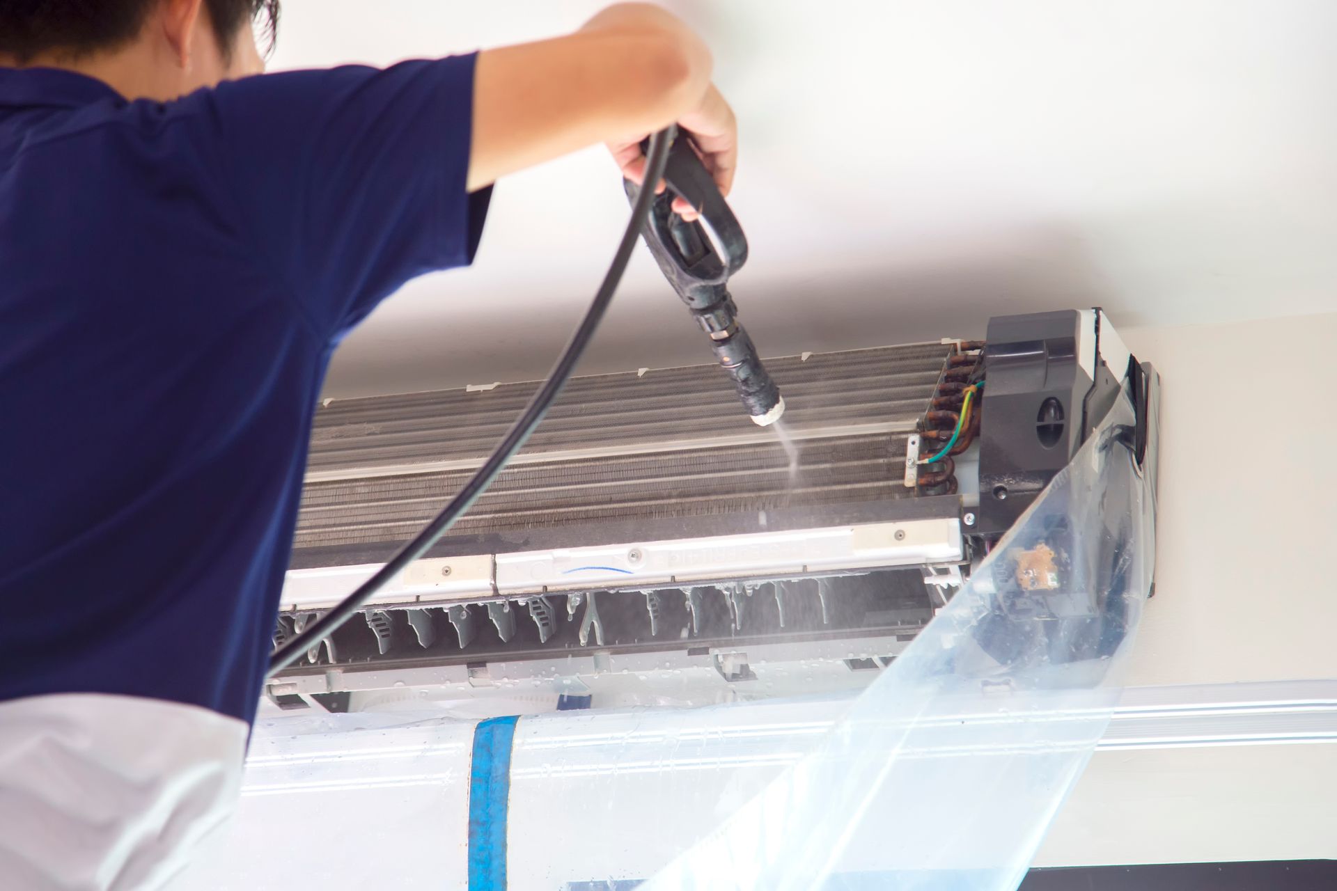 Un technicien utilise un nettoyeur à haute pression pour nettoyer les serpentins de refroidissement internes d'un climatiseur mural.