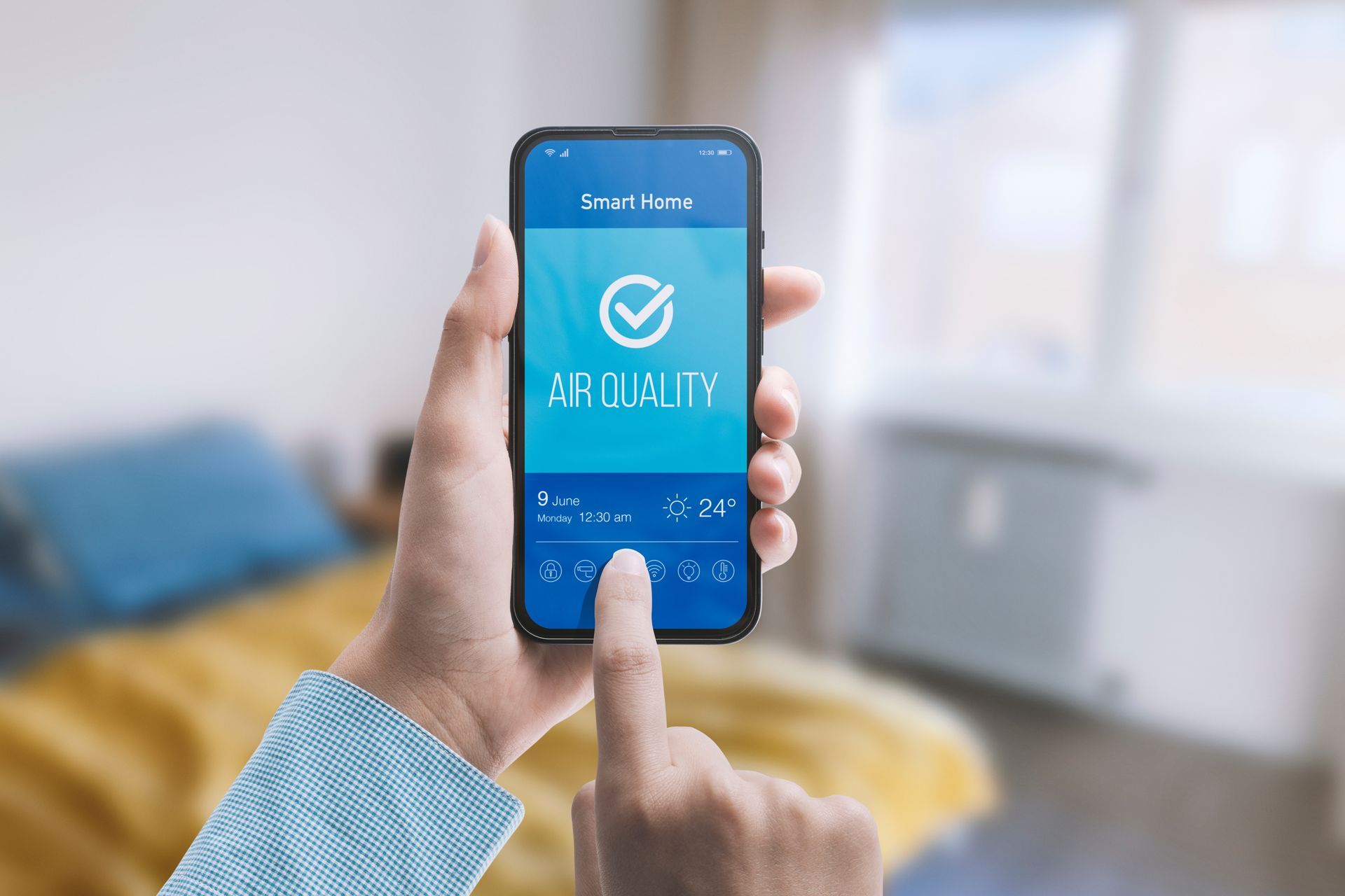 Une personne tient un smartphone affichant une application de qualité de l'air avec un symbole de coche, sur un fond de chambre flou.