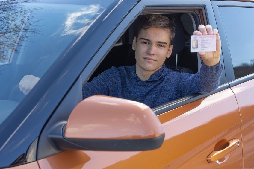 Un joven está sentado en un coche con un permiso de conducir en la mano.