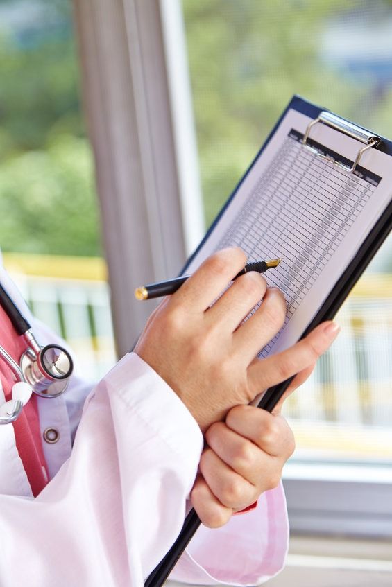 Un médico está escribiendo en un portapapeles con un bolígrafo.