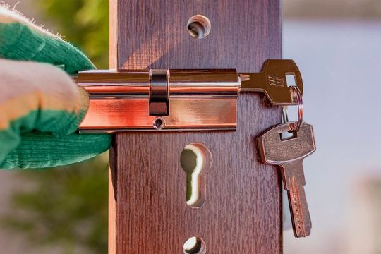 Una mano enguantada gira una llave en la cerradura de latón de una puerta de madera.