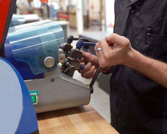 Persona utilizando una máquina azul en un banco de trabajo, ajustando una herramienta con ambas manos.
