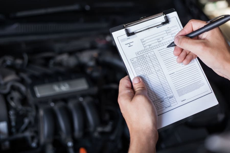Una persona está escribiendo en un portapapeles frente al motor de un automóvil.