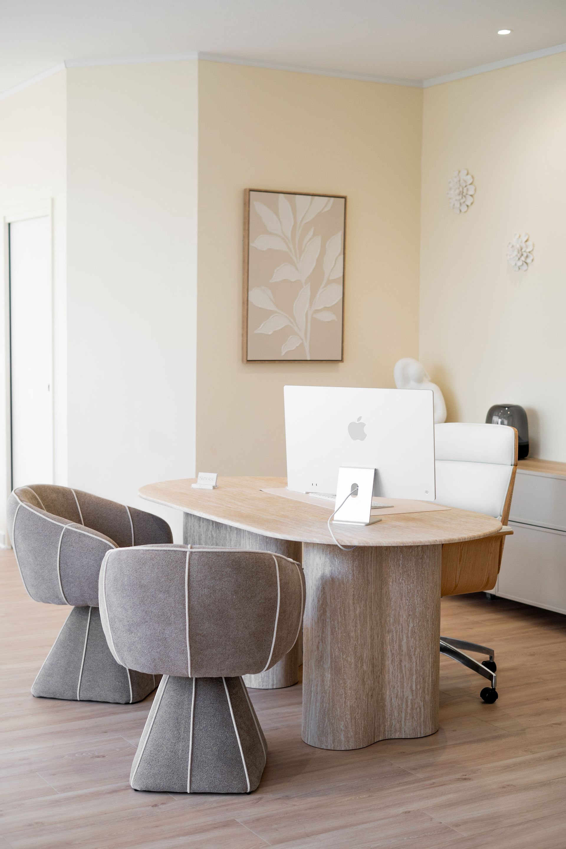 Bureau à domicile moderne avec un bureau incurvé, des chaises grises et un ordinateur, dans une pièce beige lumineuse