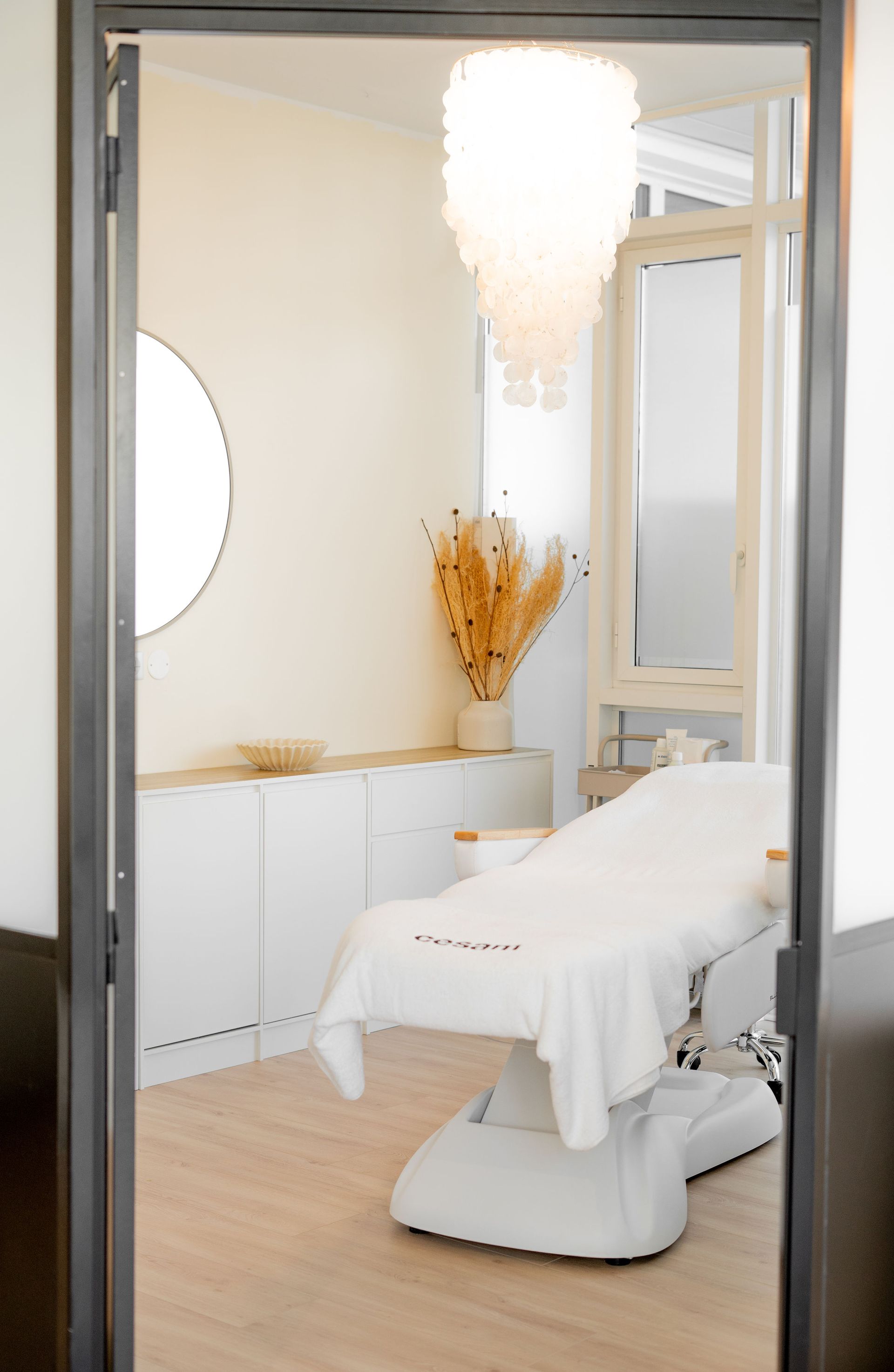 Salle de spa lumineuse et épurée, avec une table de soin, un miroir, une suspension et des meubles blancs