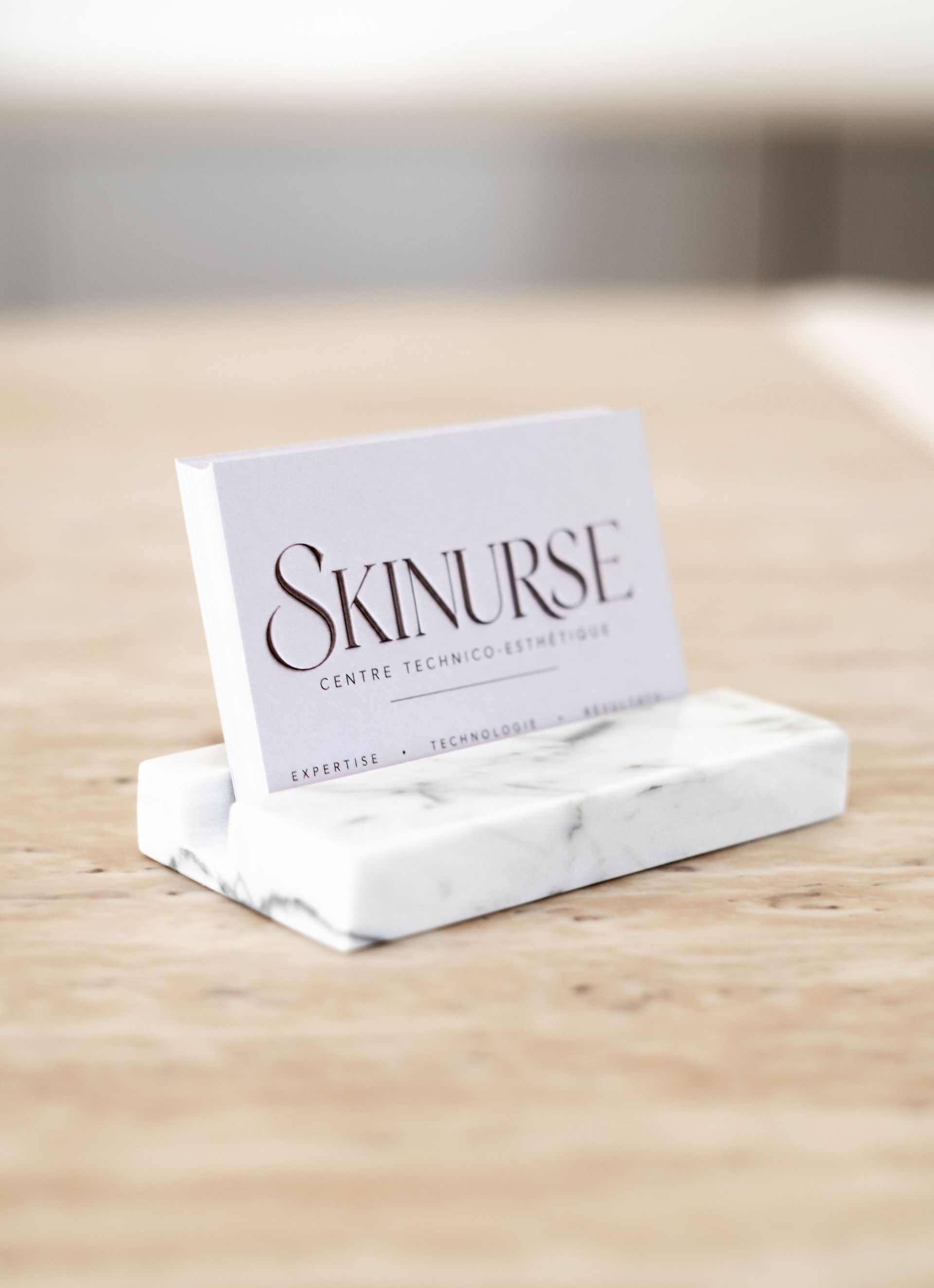 Carte de visite SKINURSE posée sur un support en marbre blanc, sur une table en bois